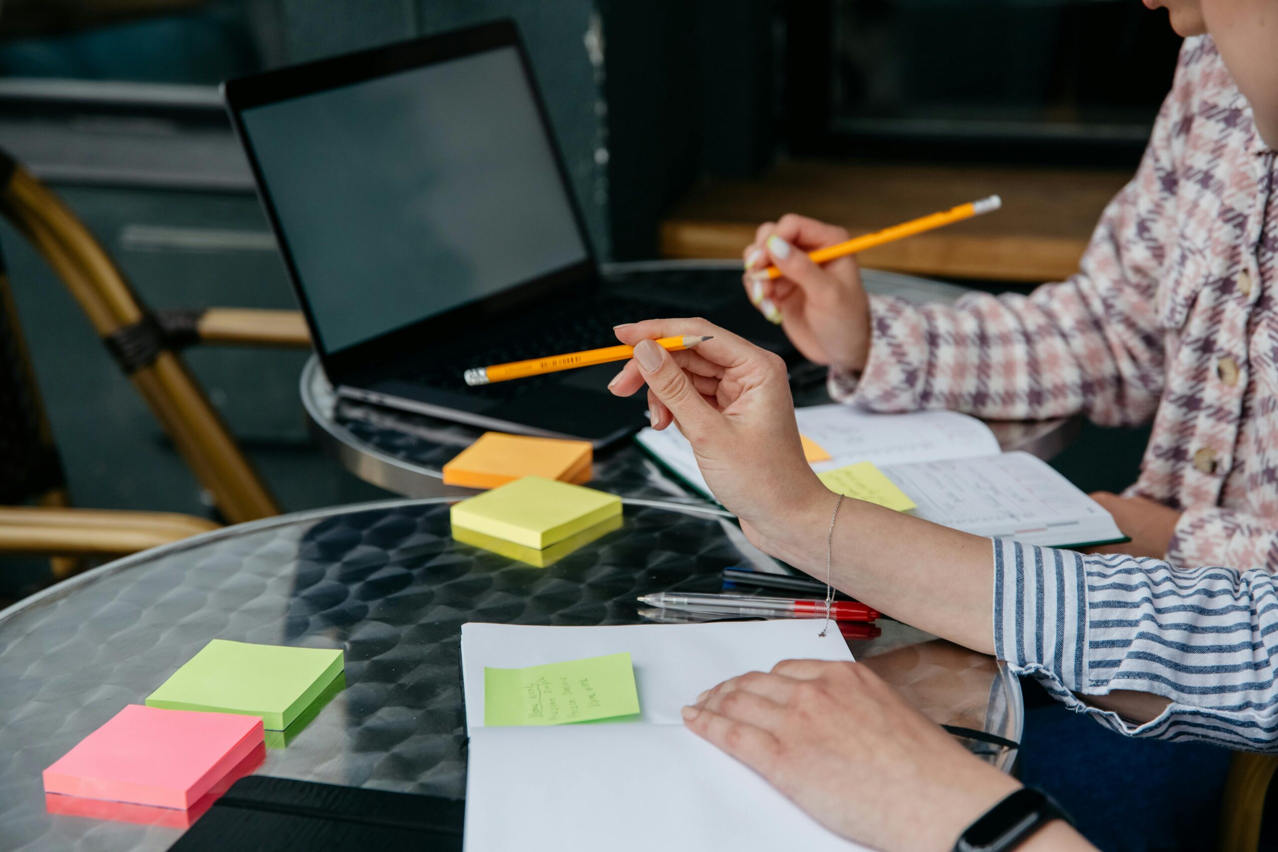 Ein Laptop auf einem Tisch, mit zwei Personen, die eine Planung eines Projektes durchführen.